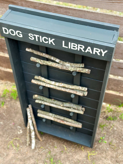 Dog pulling stick from grey Dog Stick Library in backyard